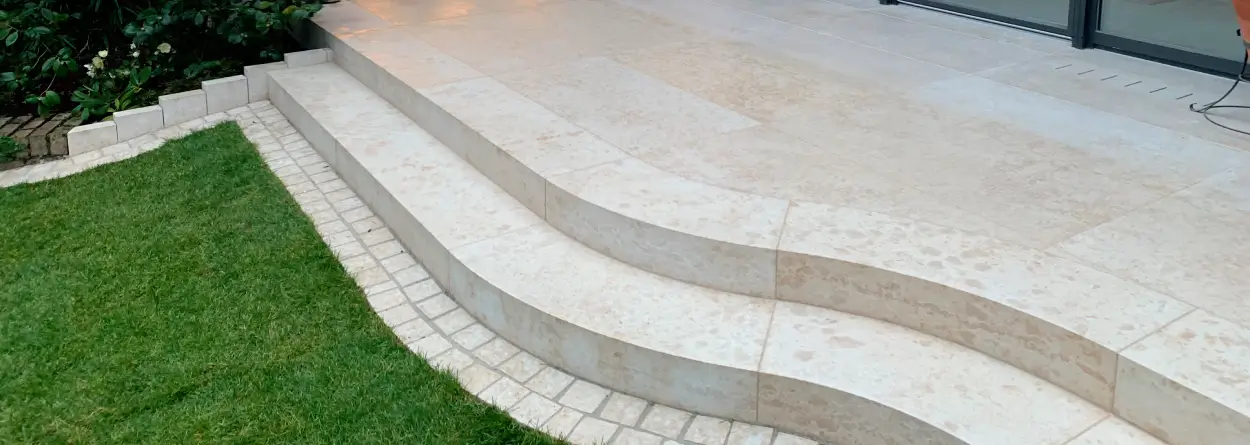 Geschwungene Blockstufen aus hellem Naturstein an moderner Terrasse mit Rasenanschluss