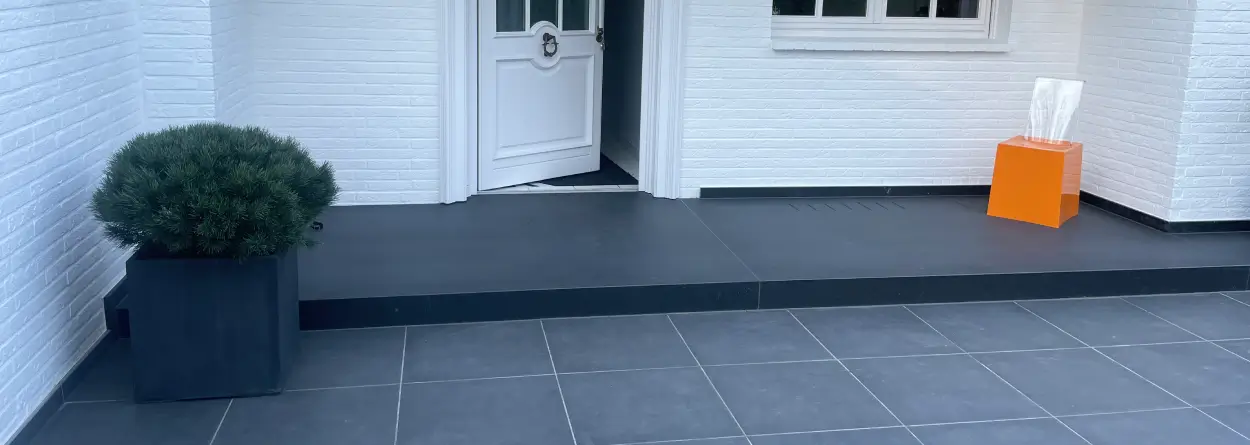 Hauseingang mit dunklen Naturstein-Bodenplatten und Blockstufen vor weißer Hausfassade