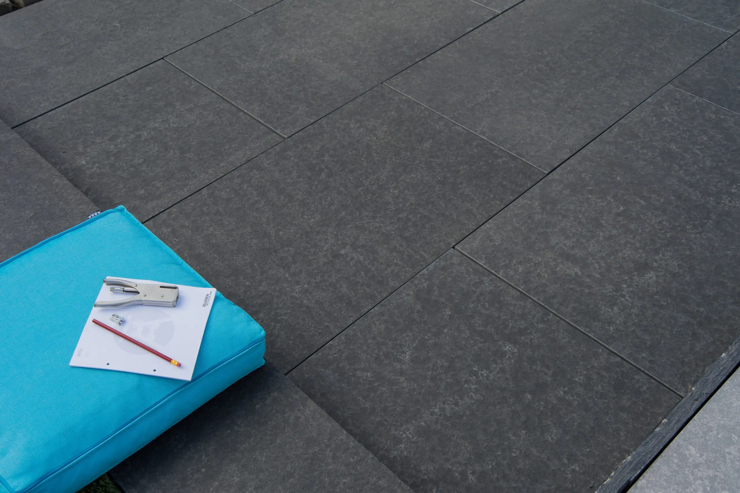 Dunkle Bodenplatten im modernen Terrassendesign mit blauem Sitzkissen.