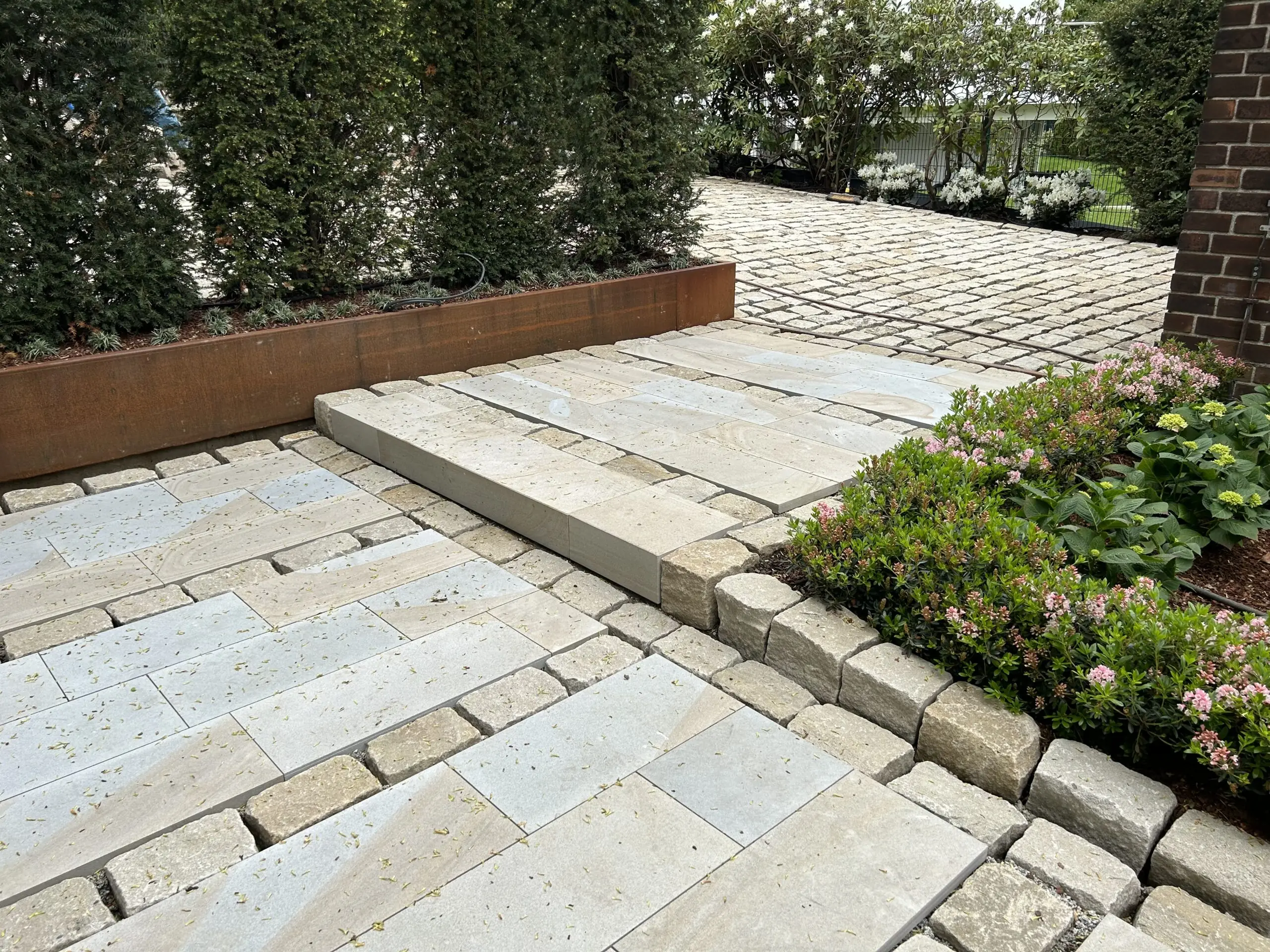 Eingangsbereich mit Natursteinplatten, Pflastersteinen und bepflanztem Blumenbeet.
