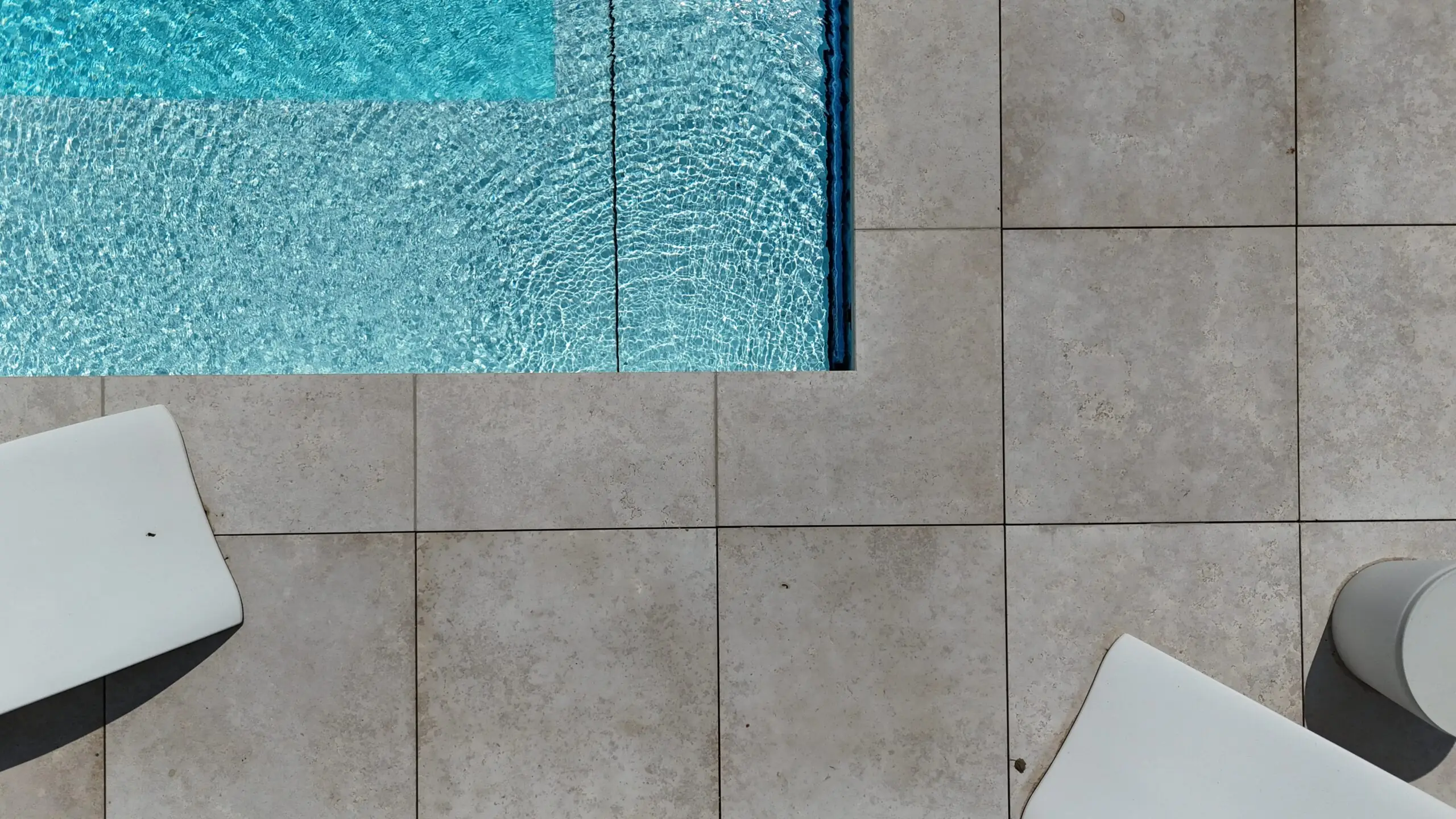 Poolumrandung mit hellen Natursteinfliesen und moderner Outdoor-Gestaltung.