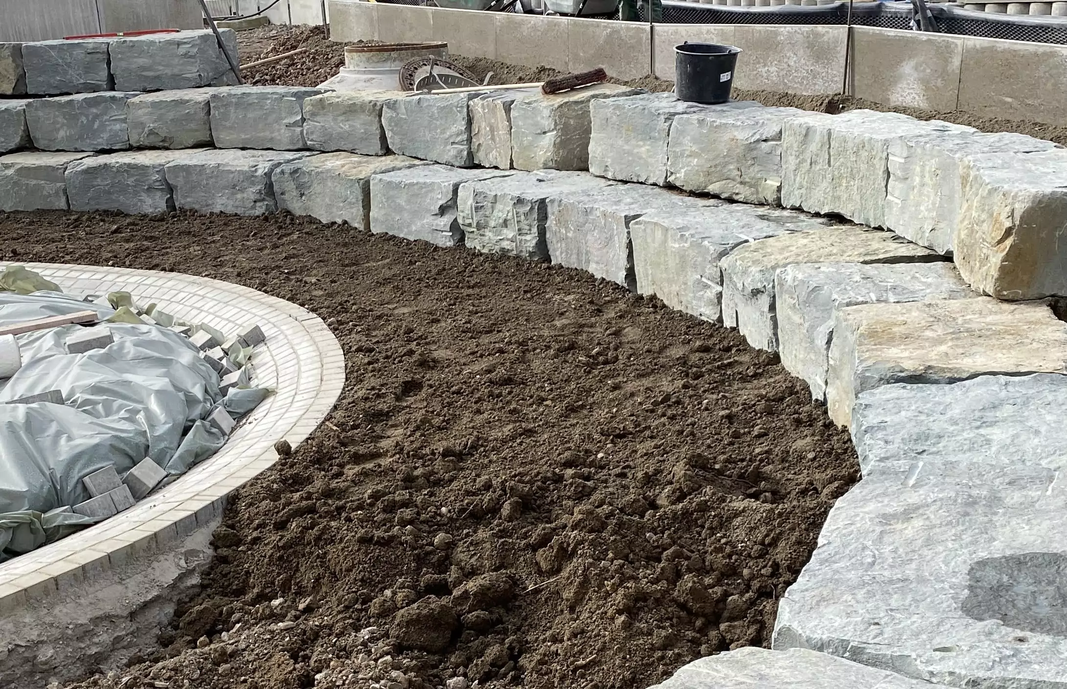 Massive Natursteinblöcke als halbrunde Stützmauer im Gartenbau.