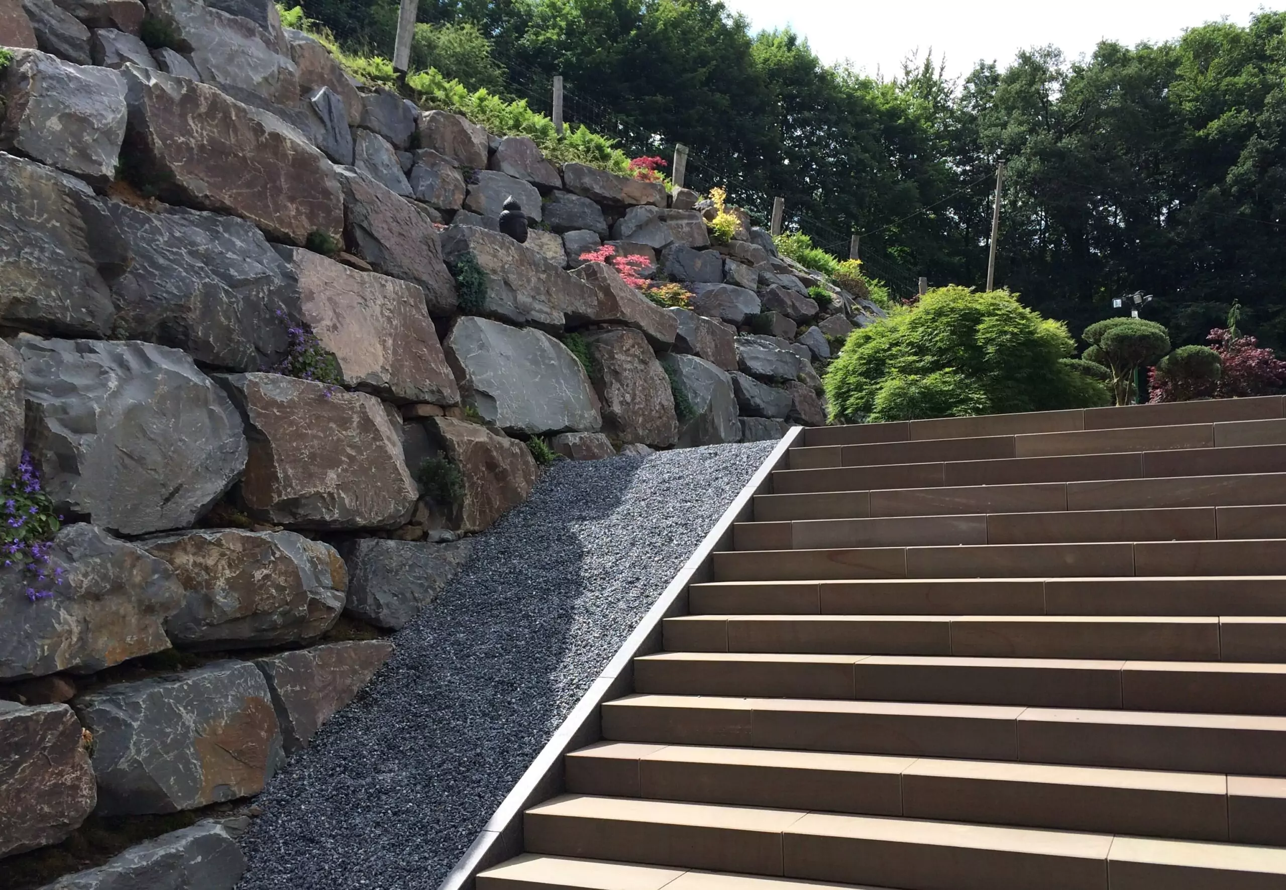 Massive Bruchsteinmauer als Hangsicherung neben moderner Gartentreppe.