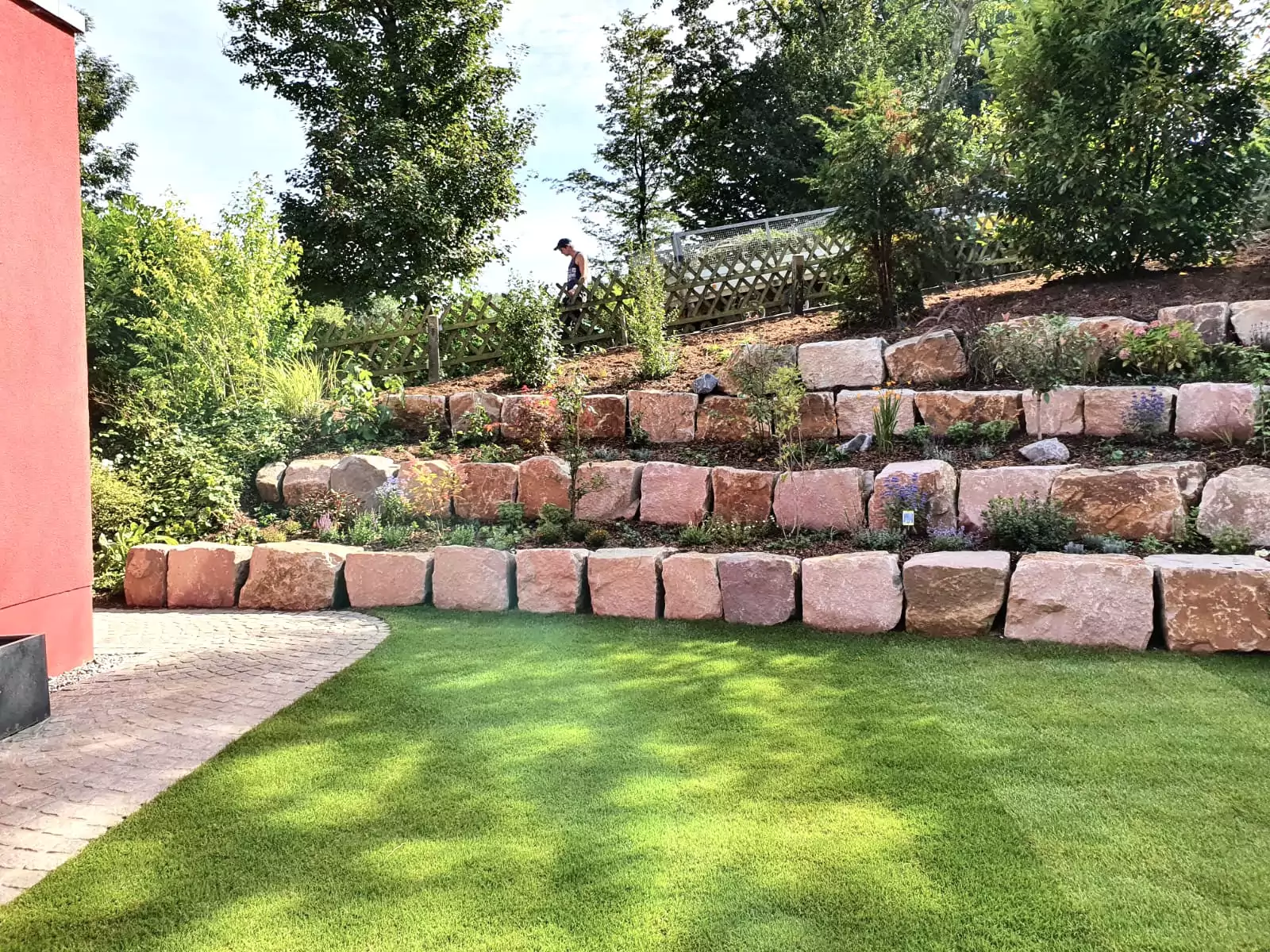 Terrassierte Gartenanlage mit roten Quadersteinen als Stützmauer und bepflanzten Ebenen.