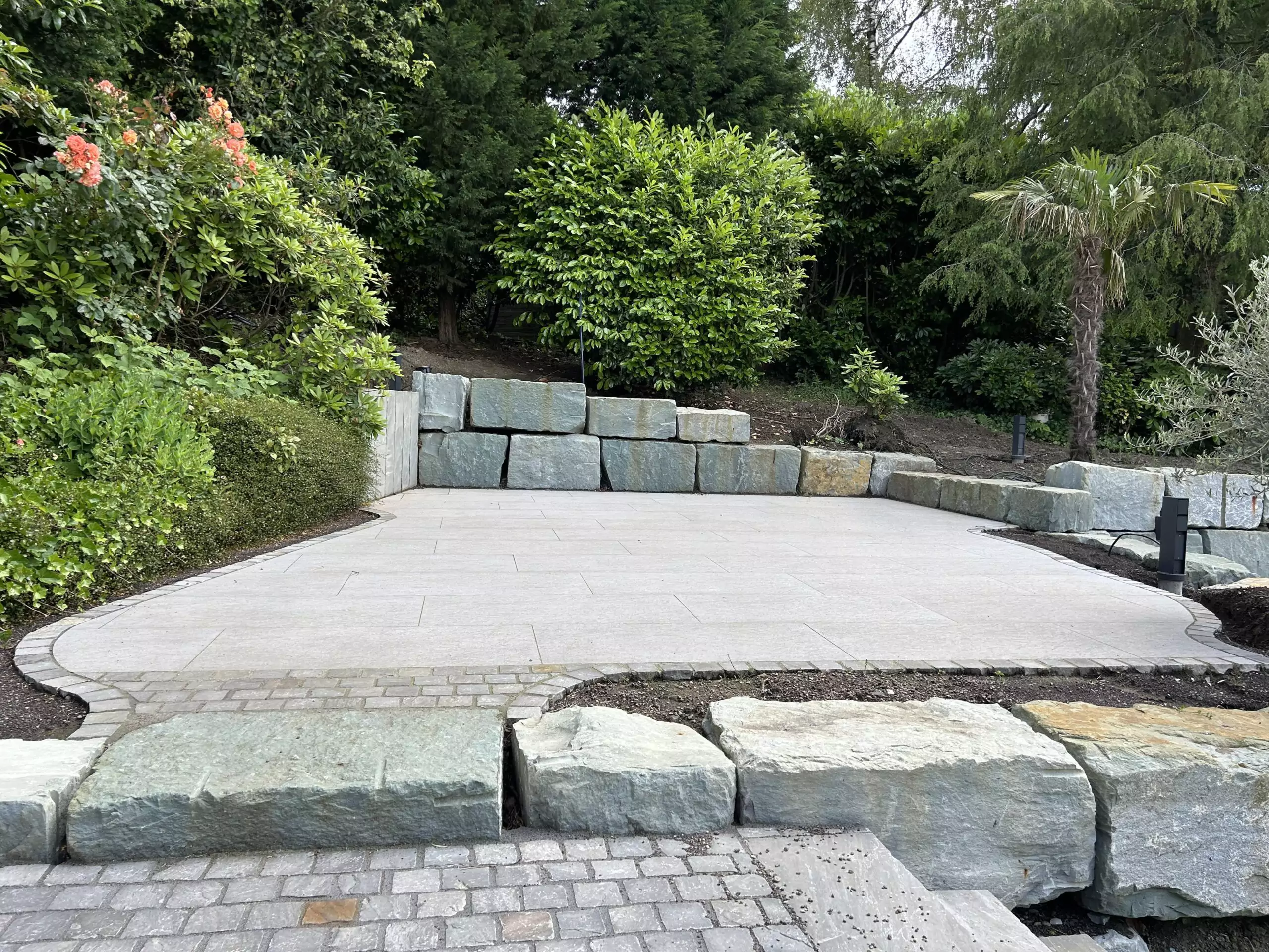 Blocksteine als stabile Stützmauer mit gepflasterter Fläche im Garten.