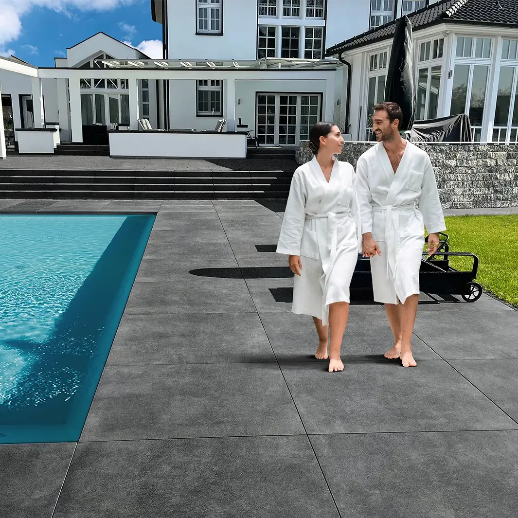 Modern gestalteter Poolbereich mit großformatigen, dunklen Keramikplatten und elegantem Wohnhaus im Hintergrund