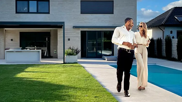 Elegantes Paar spaziert an modernem Pool mit hellen Terasssenfliesen im Garten eines Einfamilienhauses