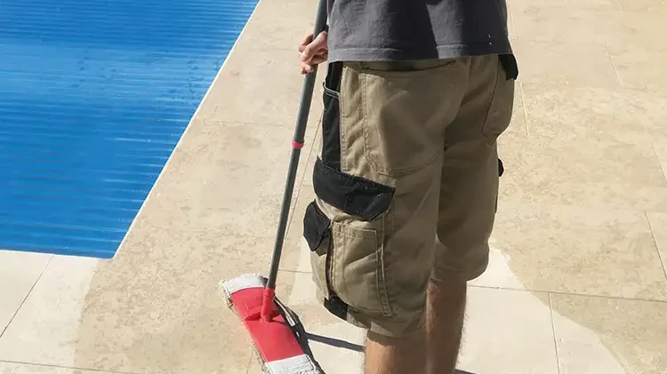Reinigung von hellen Natursteinplatten rund um den Pool mit einem Bodenwischer
