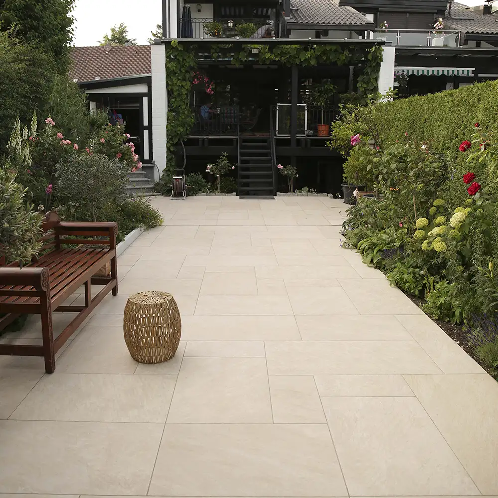 Moderne Terrasse mit hellem Feinsteinzeug im Römischen Verband neben bepflanzter Gartenfläche