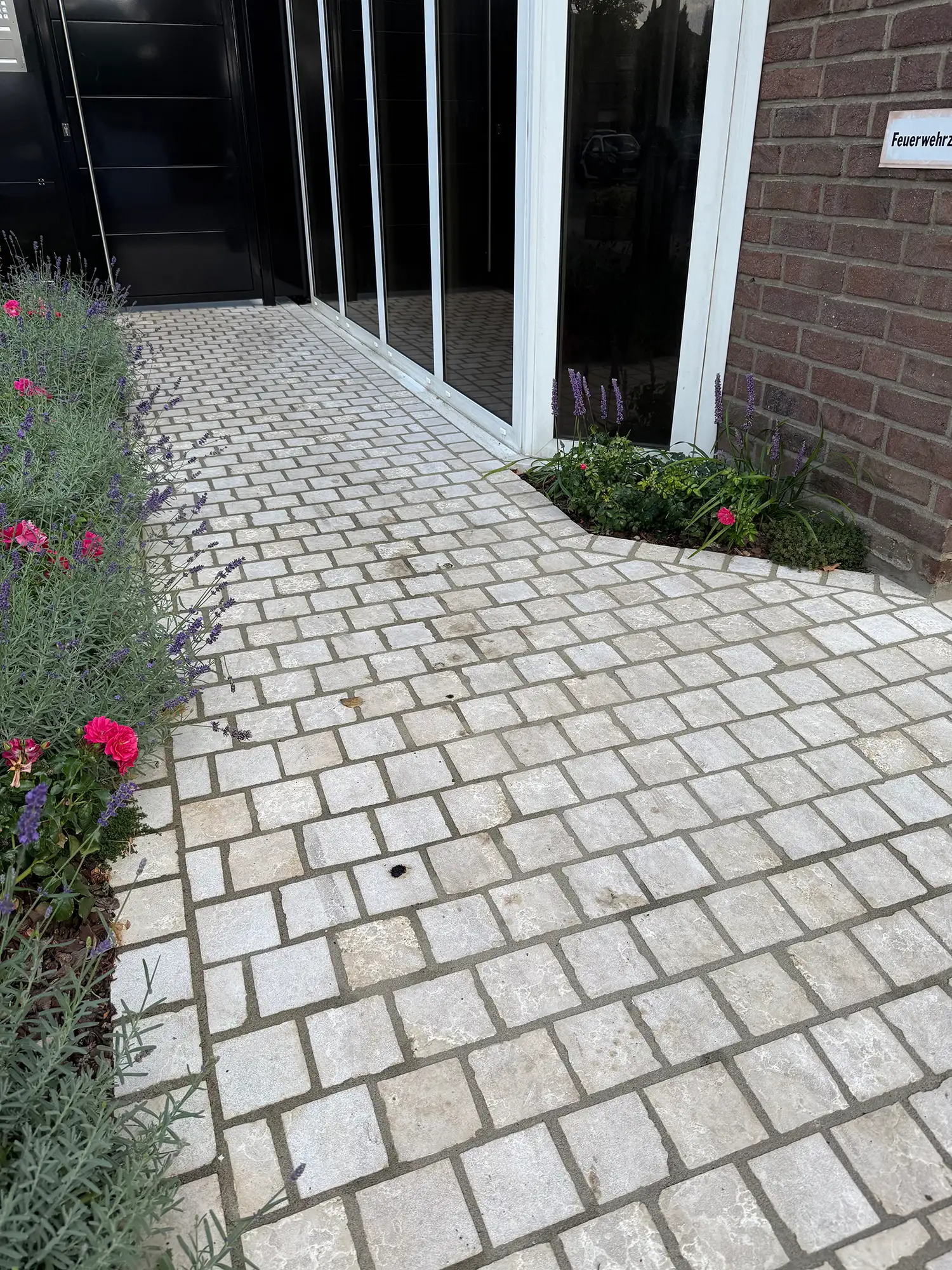 Pflastersteine aus Naturstein am Hauseingang mit hellem Kalksteinpflaster und Beetbepflanzung