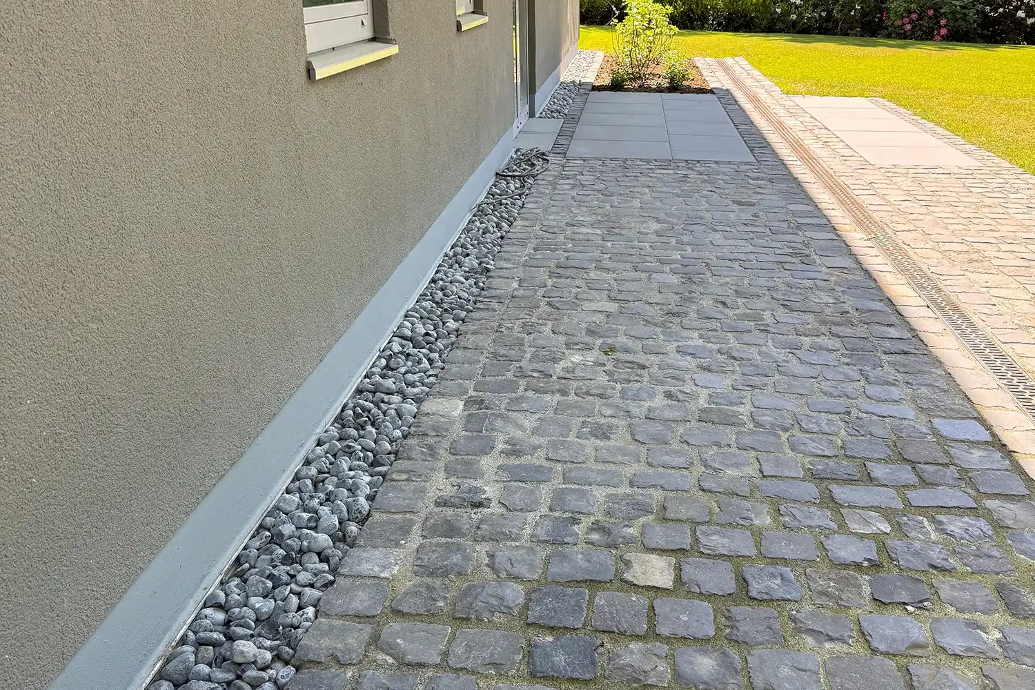 Natursteinpflaster Gartenweg aus Basalt Kleinpflaster entlang einer Hausfassade