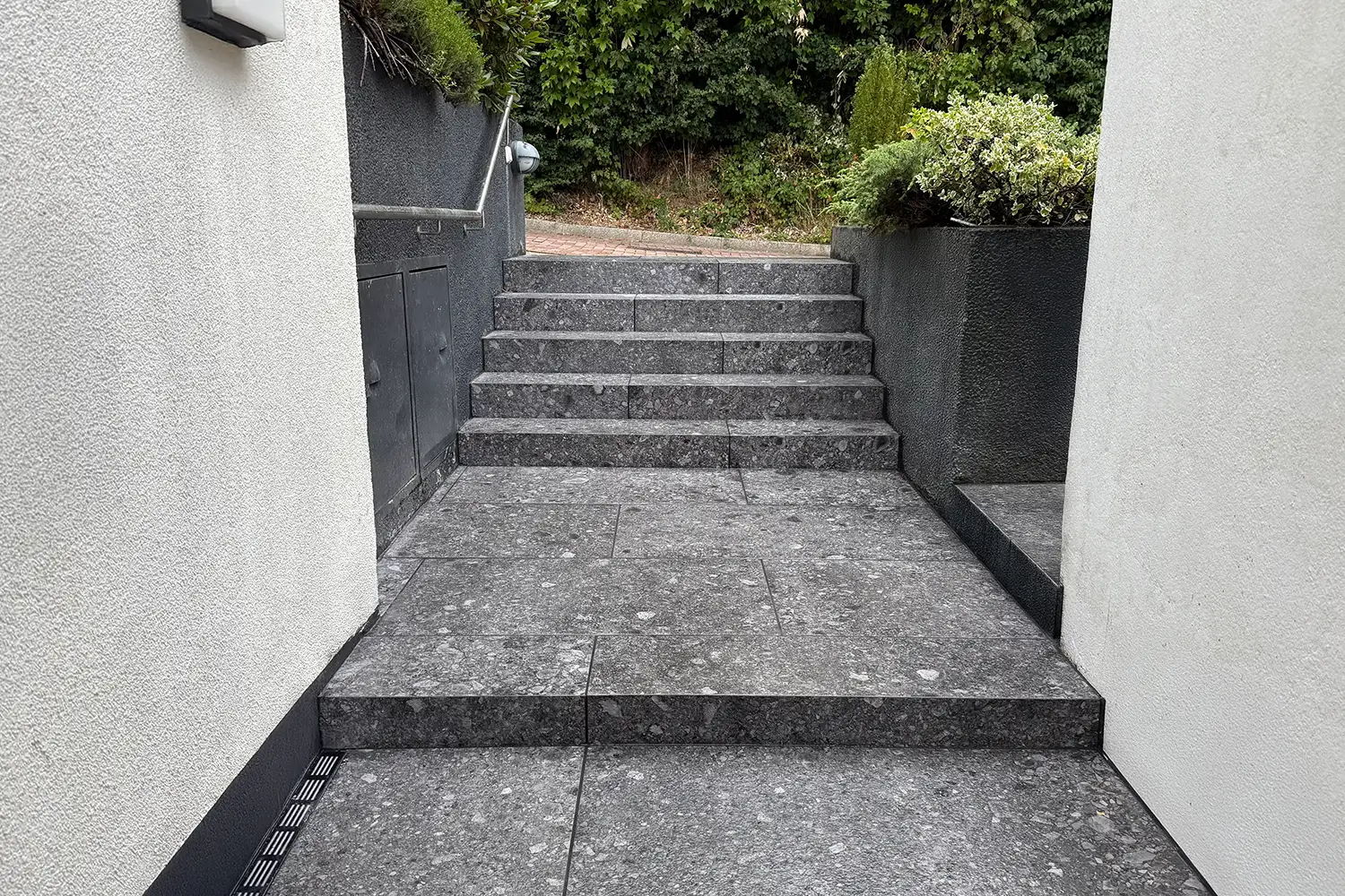 Nachher-Foto sanierte Außentreppe mit dunkelgrauen Granitplatten mit Kristallstruktur, einheitlichem Belag auf Stufen und Bodenbereich am Hauseingang