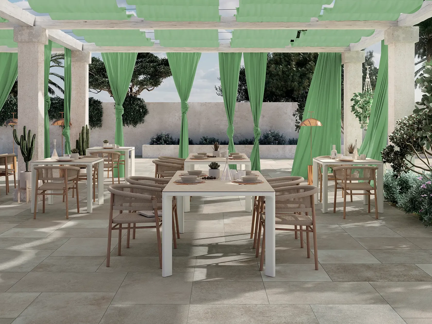 Mediterrane Restaurantterrasse unter weißer Pergola mit grünen Vorhängen auf großformatigen Keramikplatten in Betonoptik mit Rattan-Stühlen