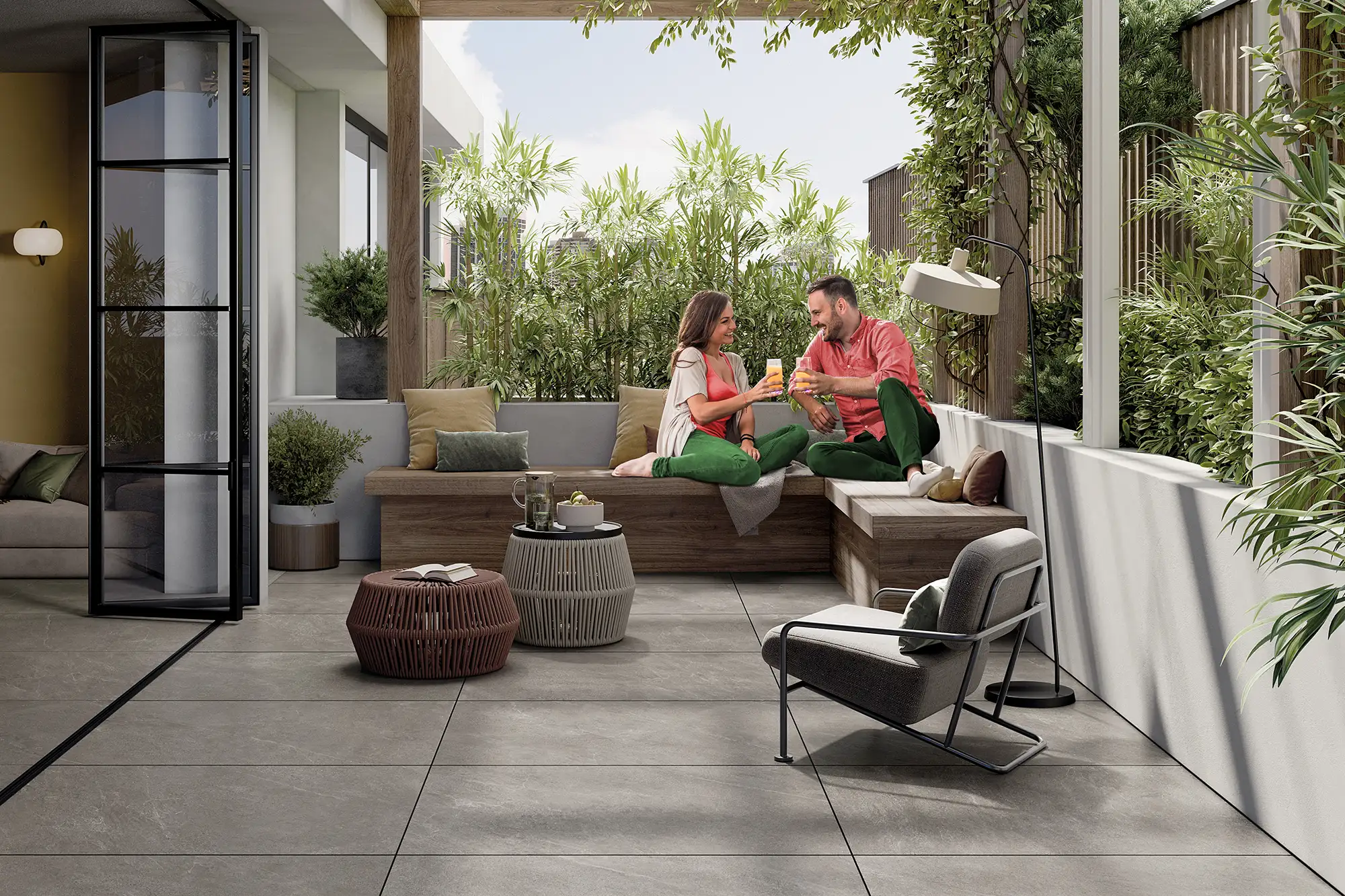 Pärchen auf urbaner Dachterrasse mit großformatigen grauen Keramikplatten in Steinoptik, Holzsitzbank, Lounge-Sessel und üppiger Begrünung