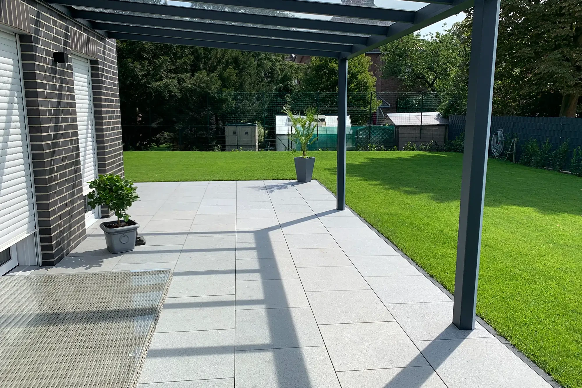 Terrasse mit Bodenplatten aus Granit Norit Naturstein unter moderner Pergola