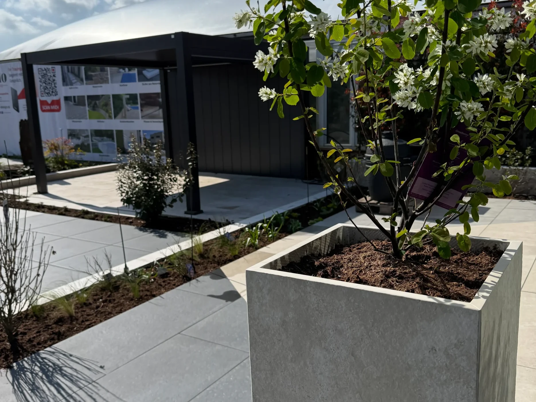 Keramikplatten-Hochbeet mit blühendem Ziergehölz und grauen Terrassenplatten in der Gartenausstellung avdo design Mülheim