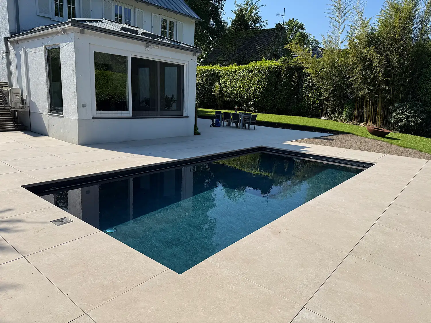 Moderne Poolumrandung mit hellen Terrassenplatten, rechteckigem Pool und großzügigem Gartenbereich
