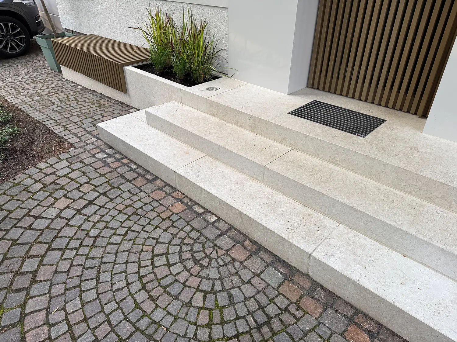 Helle Treppenstufen aus Naturstein im Eingangsbereich mit Pflasterweg, Pflanzbeet und moderner Hausfassade