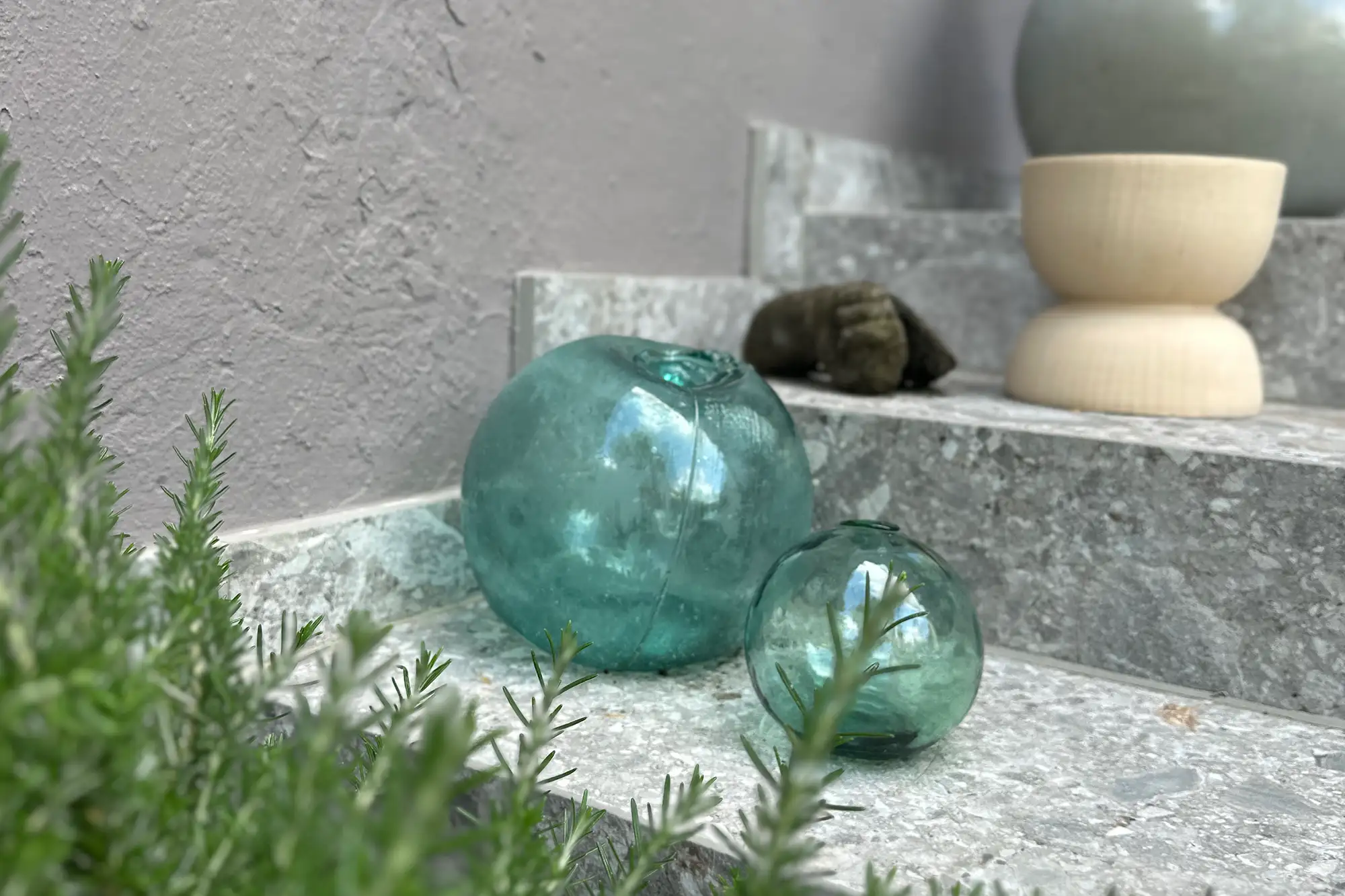 Moderne Terrasse mit grauen Natursteinplatten, dekorativen Glaselementen und mediterraner Bepflanzung