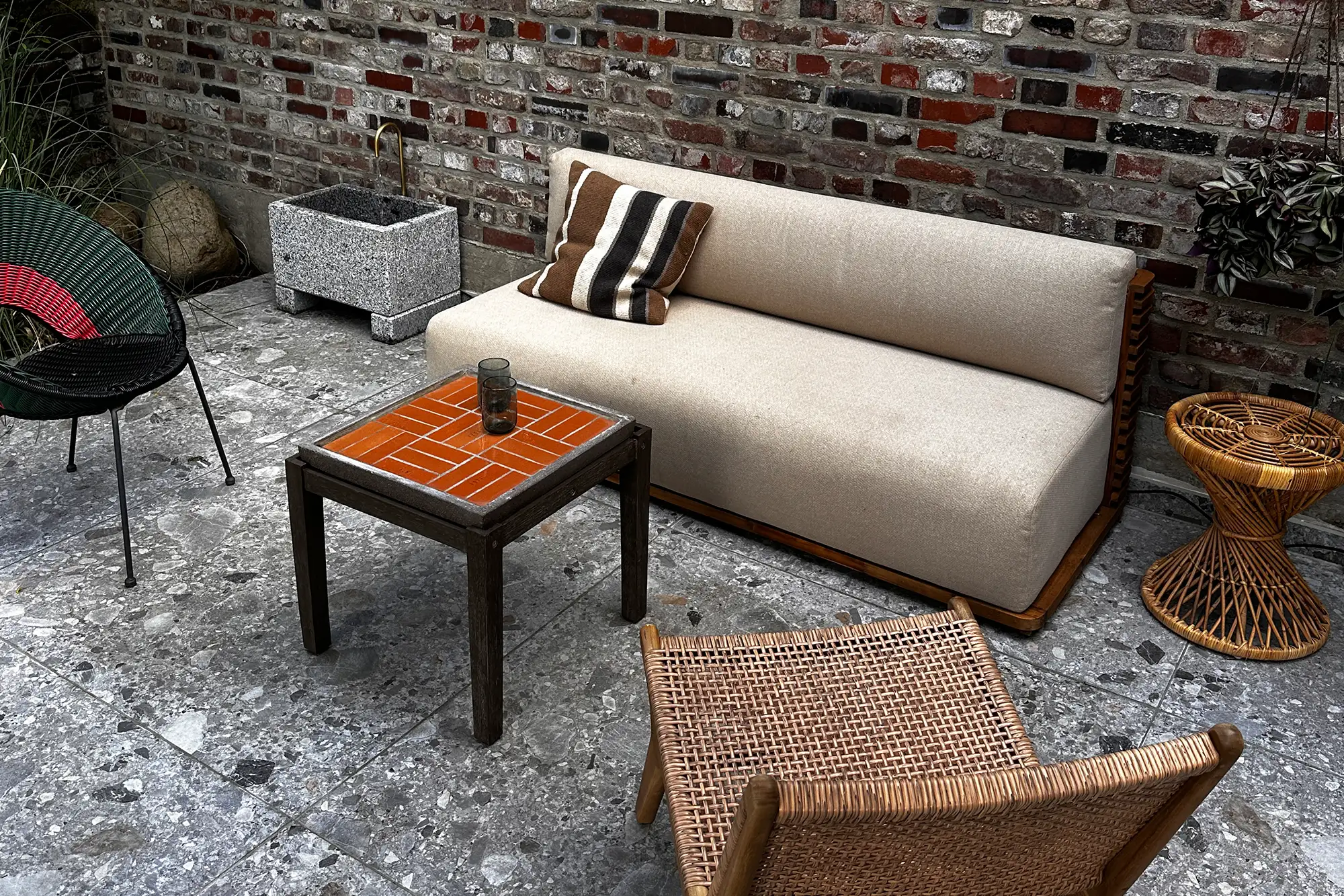 Terrassen-Lounge mit grauen Steinplatten in Terrazzo-Optik, Outdoor-Sofa, Rattanmöbeln und Klinkerwand