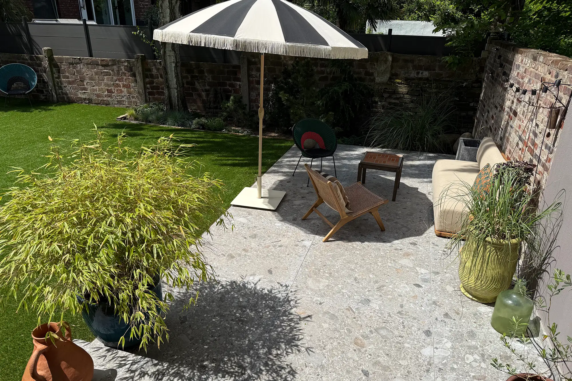 Moderne Terrasse mit grauen Steinplatten, Sonnenschirm, Outdoor-Lounge, Rasenfläche und grüner Gartenumgebung