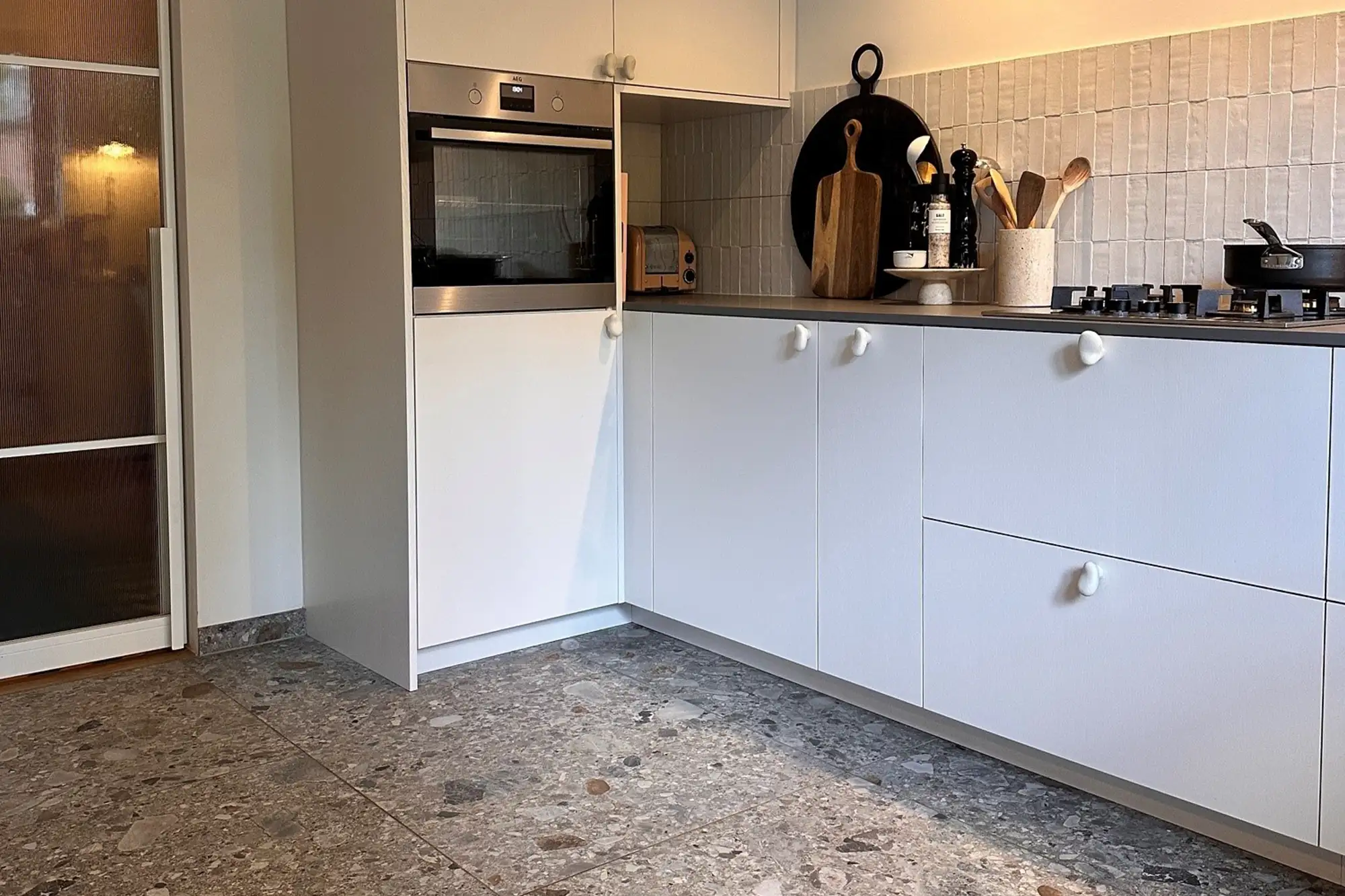 Moderne Küche mit hellen Küchenfronten, großformatigem Steinboden, gefliester Rückwand und stilvoller Arbeitsfläche