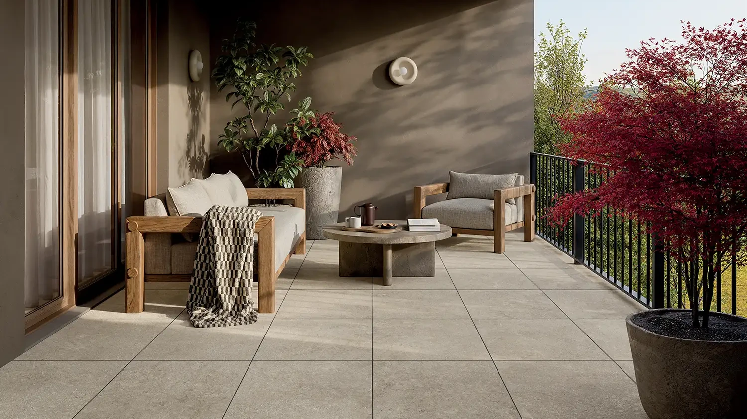 Terrasse mit grauen Keramikplatten in körniger Steinoptik, Outdoor-Sofa, Pflanzkübeln und Fächerahorn.