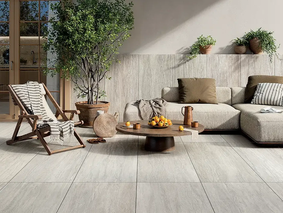 Mediterrane Terrasse mit hellgrauen Keramikplatten in Steinoptik, Holzliegestuhl, Loungesofa und Olivenbaum.
