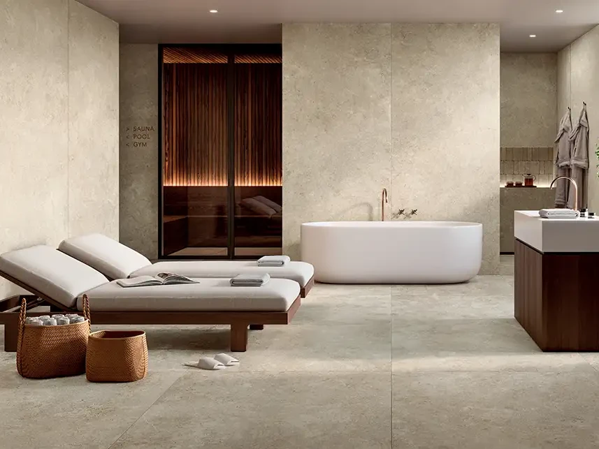 Modernes Spa-Bad mit beigen Keramikplatten in Steinoptik, freistehender Badewanne, Sauna und Ruheliegen.