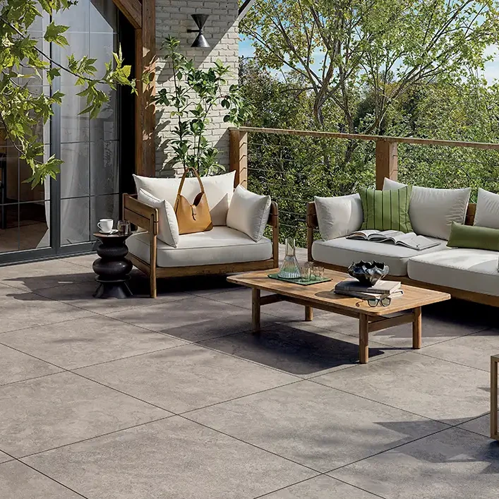 &Uuml;berdachte Terrassen-Lounge mit grauen Keramikplatten in Steinoptik, gepolsterten Sofas und Pflanzen am Holzpaneel.