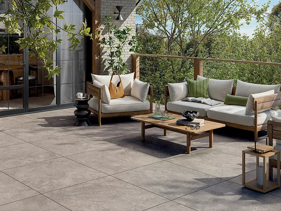 &Uuml;berdachte Terrassen-Lounge mit grauen Keramikplatten in Steinoptik, gepolsterten Sofas und Pflanzen am Holzpaneel.
