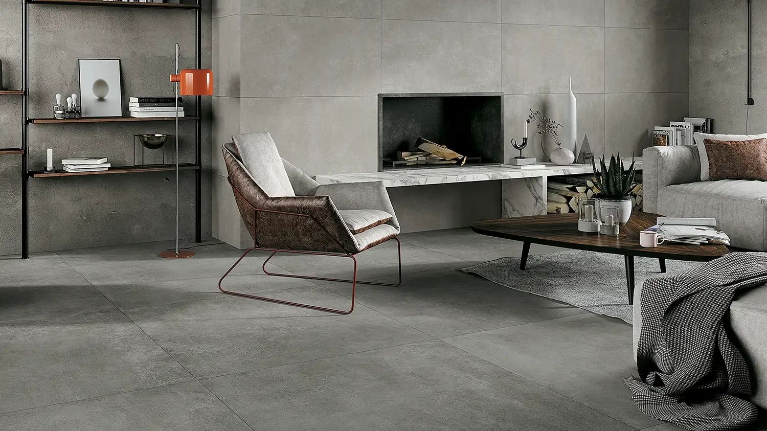 Wohnraum mit grauen Keramikplatten in Betonoptik, Loungesesseln, Kamin und offenem Regalsystem.