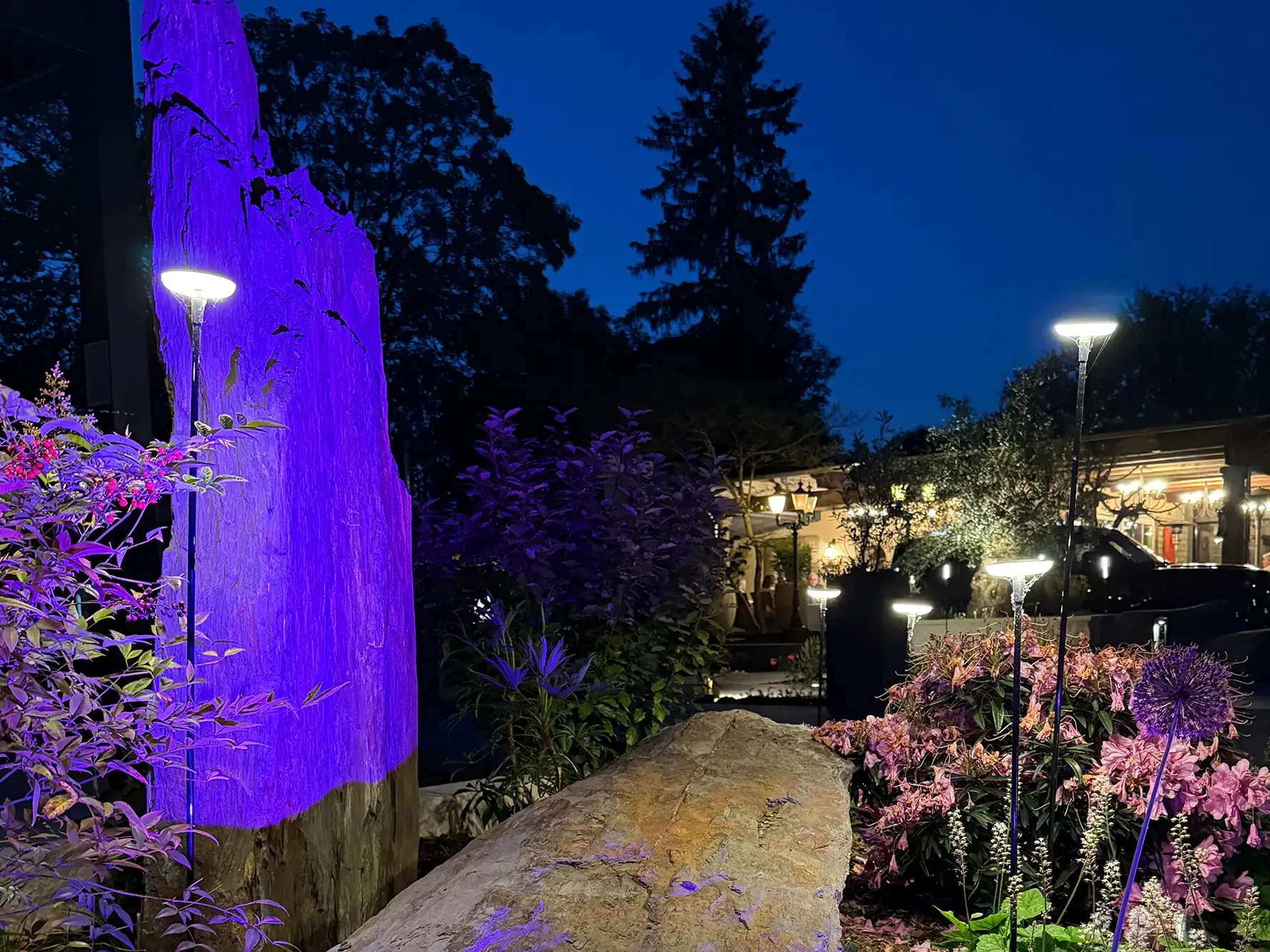 Beleuchteter Naturstein in der avdo design Gartenausstellung mit Gartenleuchten, Pflanzen und moderner Außenbeleuchtung bei Nacht