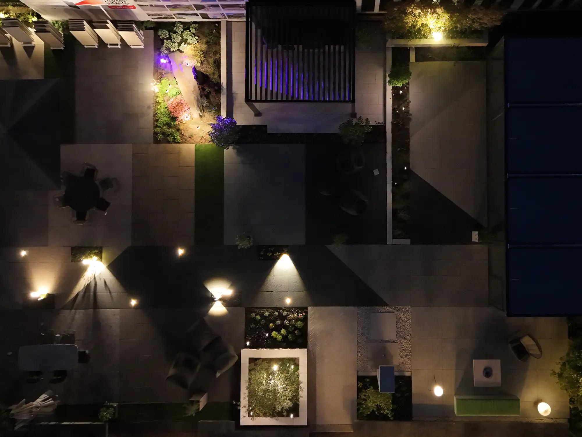 Beleuchtete Gartenausstellung von avdo design mit Naturstein, Keramikplatten, Pflanzbereichen und moderner Außenbeleuchtung bei Nacht
