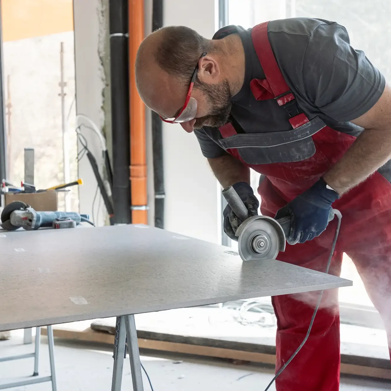 Handwerker schneidet eine Feinsteinzeugplatte mit Winkelschleifer und Diamantscheibe.