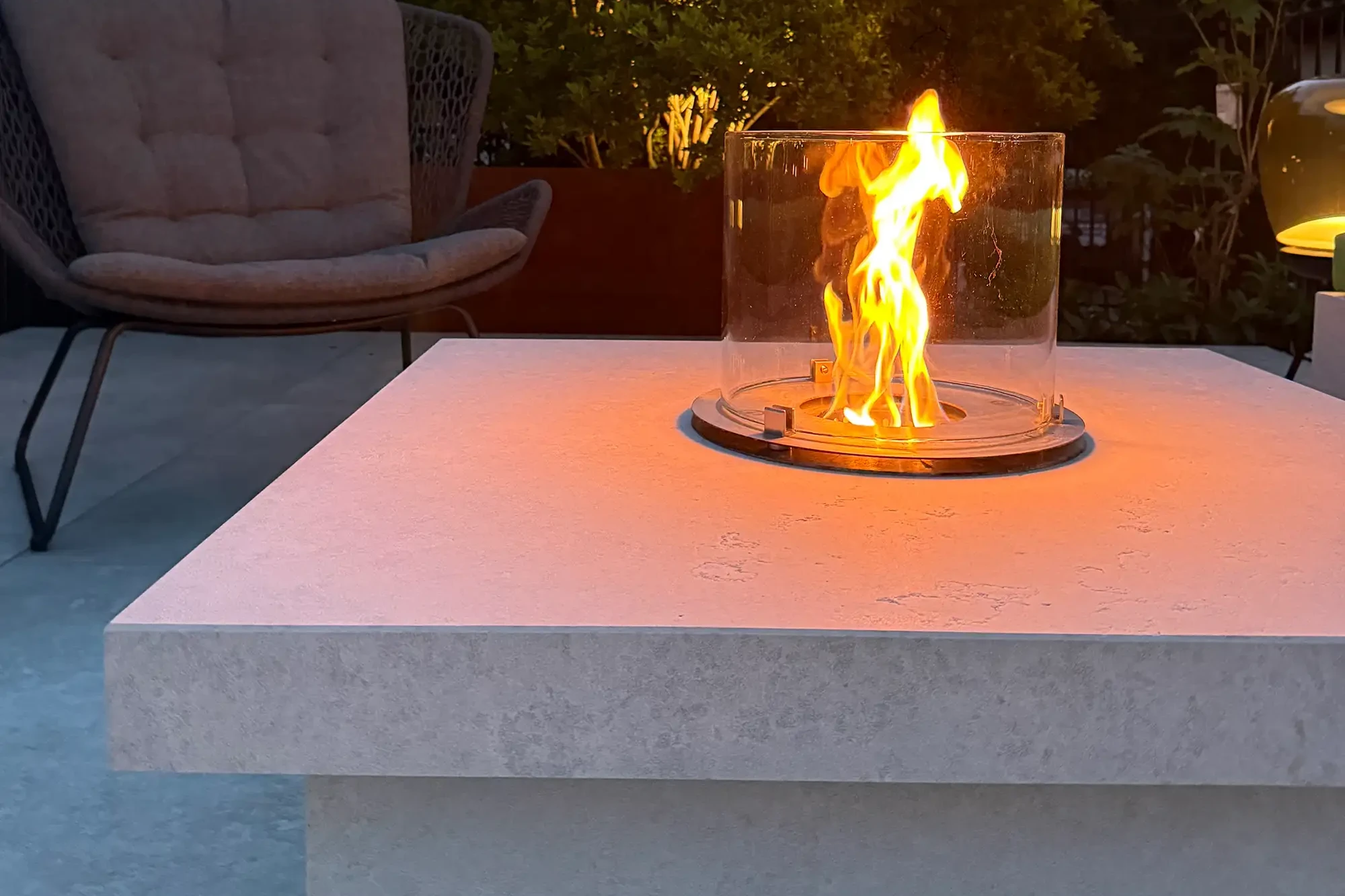 Detailaufnahme eines Kamintischs mit Glas-Windschutz, Flamme und Naturstein-Abdeckplatte.