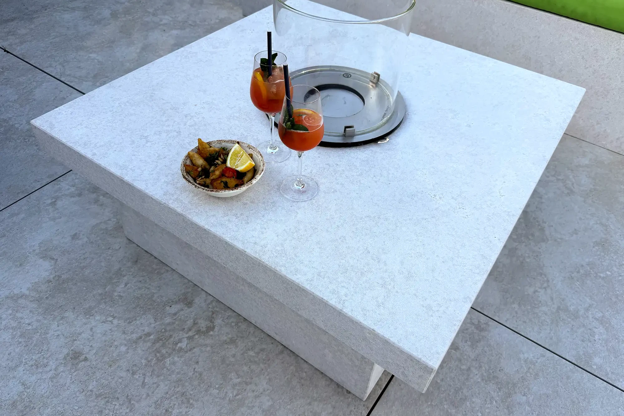 Kamintisch aus Kanfanar-Kalkstein mit Glas-Windschutz, Getränken und Snacks auf einer Terrasse.