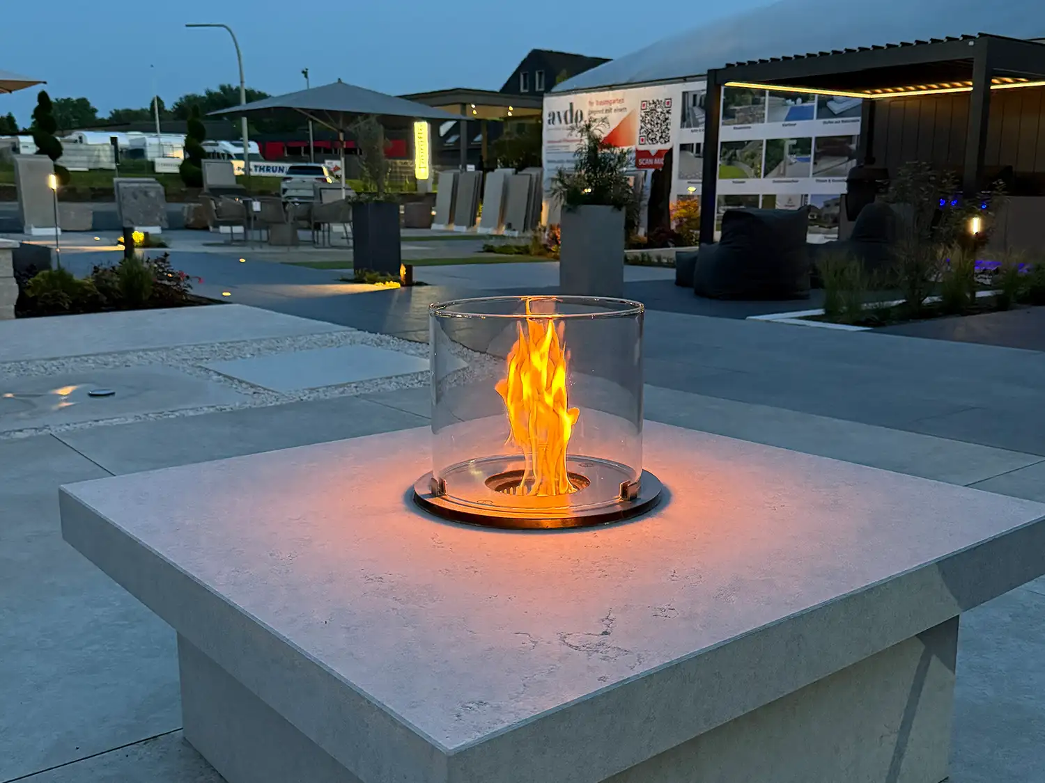 Kamintisch aus Kanfanar-Kalkstein mit Glas-Windschutz und Flamme in moderner Gartenausstellung.